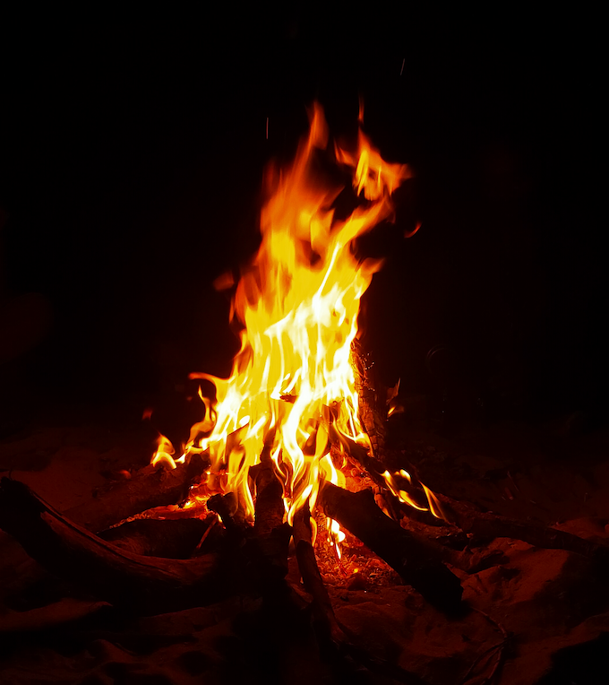 A solitary bonfire glowing brightly in the darkness, its flames dancing against a black night background.